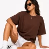 Woman wearing oversized brown cotton t-shirt with white shorts and sneakers, casual streetwear outfit