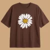 Woman wearing oversized brown daisy print t-shirt with white denim shorts, casual streetwear style