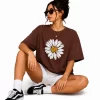 Woman wearing oversized brown daisy print t-shirt with white denim shorts, casual streetwear style