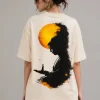 Front view: "Woman wearing beige oversized t-shirt with 'Find Peace Within' text print, front view" Back view: "Woman wearing beige oversized t-shirt with Buddha silhouette sunset graphic print on back"