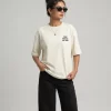 Front view: "Woman wearing beige oversized t-shirt with 'Find Peace Within' text print, front view" Back view: "Woman wearing beige oversized t-shirt with Buddha silhouette sunset graphic print on back"