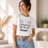 Woman wearing white cropped t-shirt with printed cat face "meow" graphic design and pink heart print, paired with blue jeans