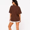 Woman wearing oversized brown cotton t-shirt with white shorts and sneakers, casual streetwear outfit