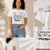 Woman wearing white cropped t-shirt with printed cat face "meow" graphic design and pink heart print, paired with blue jeans