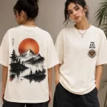 Woman wearing beige oversized t-shirt with Japanese ink-style mountain and red sun print on back, 'Find Peace Within' text with medallion graphic on front