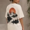 Woman wearing beige oversized t-shirt with Japanese ink-style mountain and red sun print on back, 'Find Peace Within' text with medallion graphic on front