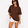 Woman wearing oversized brown cotton t-shirt with white shorts and sneakers, casual streetwear outfit