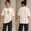 Woman wearing beige oversized Samurai graphic t-shirt with red Japanese kanji print, paired with black wide-leg jeans front and back view