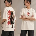 Woman wearing beige oversized t-shirt with samurai warrior illustration and red Japanese kanji print on back, 'SAMURAI' text print on front, styled with black wide-leg jeans