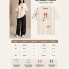 Woman wearing beige oversized t-shirt with samurai warrior illustration and red Japanese kanji print on back, 'SAMURAI' text print on front, styled with black wide-leg jeans
