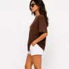 Woman wearing oversized brown cotton t-shirt with white shorts and sneakers, casual streetwear outfit