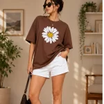 Woman wearing oversized brown daisy print t-shirt with white denim shorts, casual streetwear style