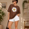 Woman wearing oversized brown daisy print t-shirt with white denim shorts, casual streetwear style