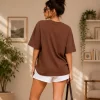 Woman wearing oversized brown daisy print t-shirt with white denim shorts, casual streetwear style