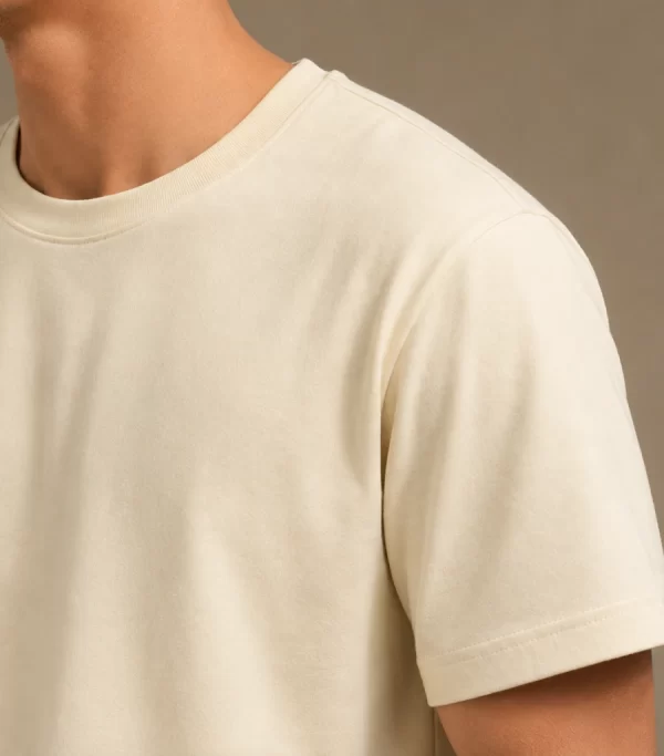 Man wearing a relaxed-fit cream t-shirt paired with khaki chinos and white sneakers, standing in a sunlit minimal interior.