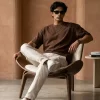 Man wearing brown oversized t-shirt with cream cargo pants, sunglasses, and white sneakers in a minimal studio setting.