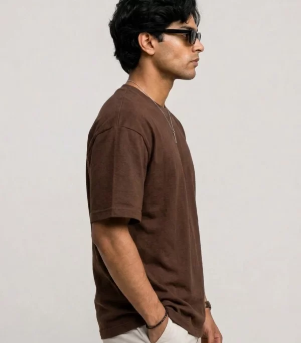 Man wearing brown oversized t-shirt with cream cargo pants, sunglasses, and white sneakers in a minimal studio setting.